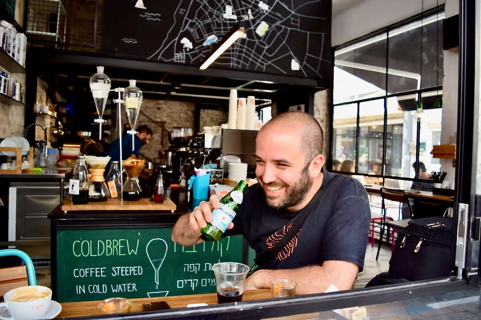 Shlomi Asaf, do Sabores de Israel, sentado em uma cafeteria, segurando uma garrafa de água nas mãos